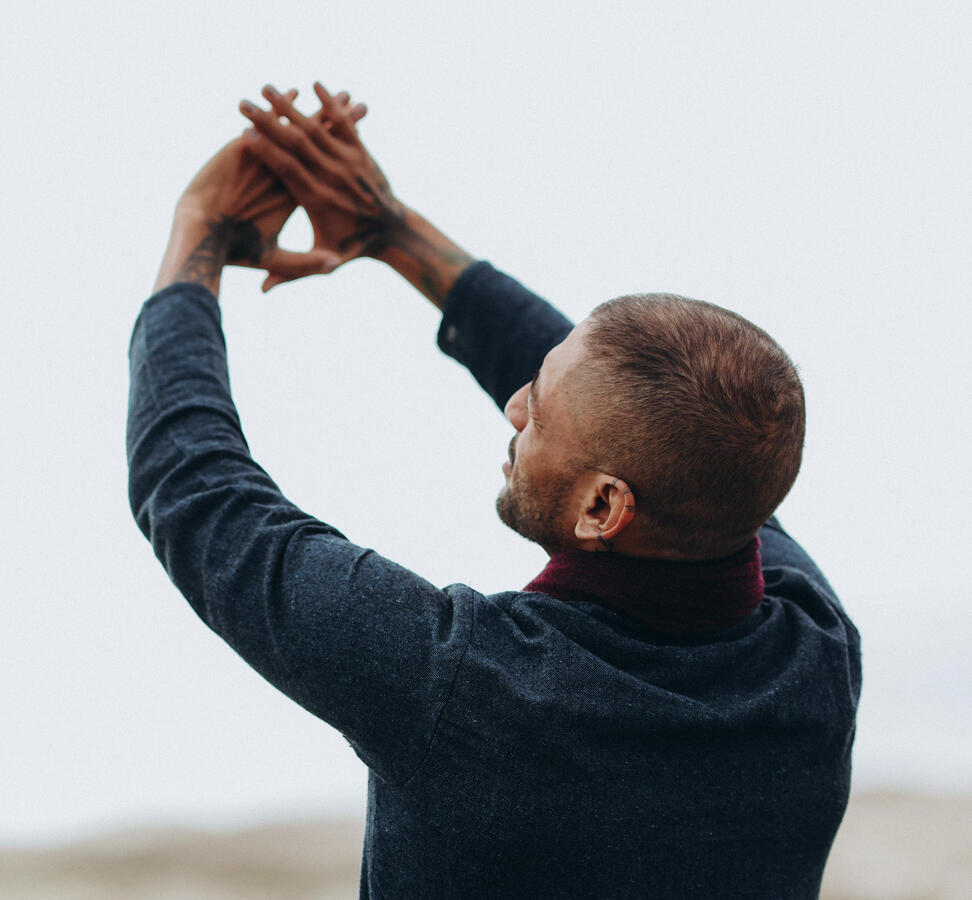 Back and side view of Free Lopez looking up at his hands extended toward the sky, embodying mindfulness, openness, and spiritual connection in a serene outdoor setting.