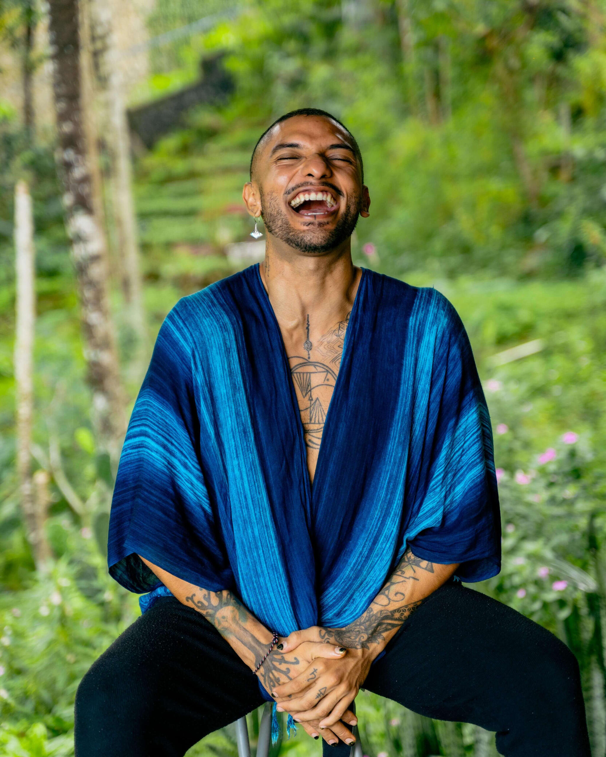 Free Lopez Free Lopez, holistic healing practitioner in Lombok, laughing in nature while wearing a blue robe — Reiki, yoga, sound healing, and coaching.