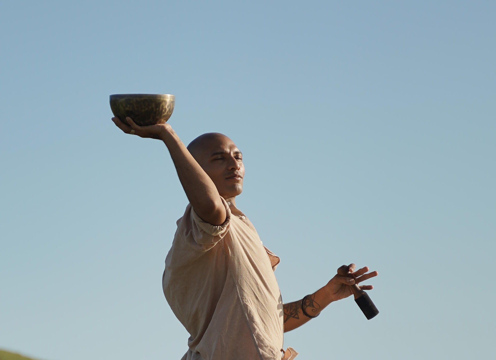 Sound Healing Trainor Free Lopez holding tibetan singing bowl Holistic Coach and Sound Healing Faciliator Free Lopez with Tibetan Singing Bowl depicted in nature with sky as background