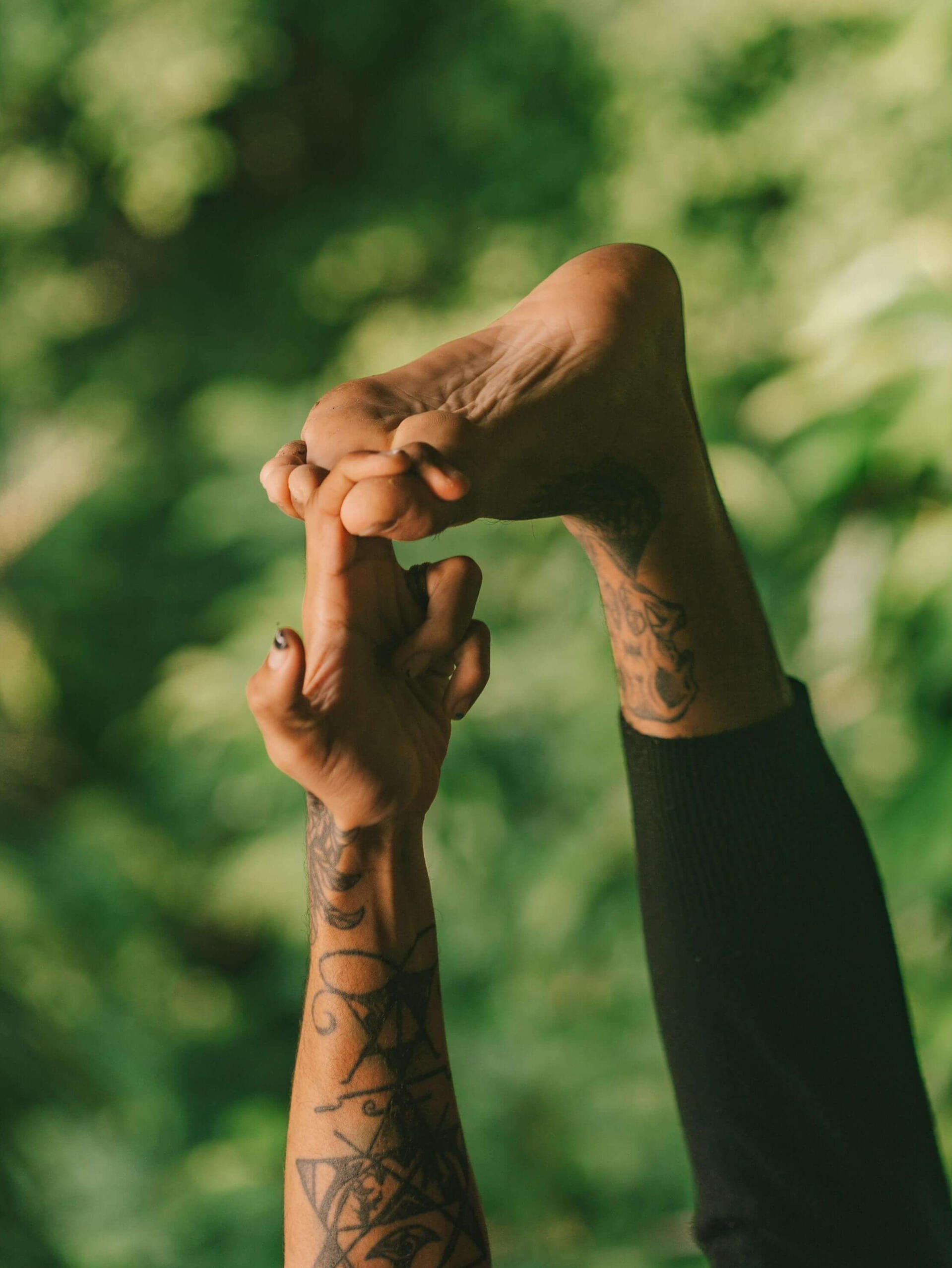 Yoga Toe Hold Pose with Hand and Foot Reaching Skyward in Tropical Garden Close-up of a hand grasping the big toe in a yoga asana, with leg extended upward toward the sky, set against a backdrop of lush tropical greenery in Lombok Indonesia, symbolizing balance, flexibility, and mindful movement.