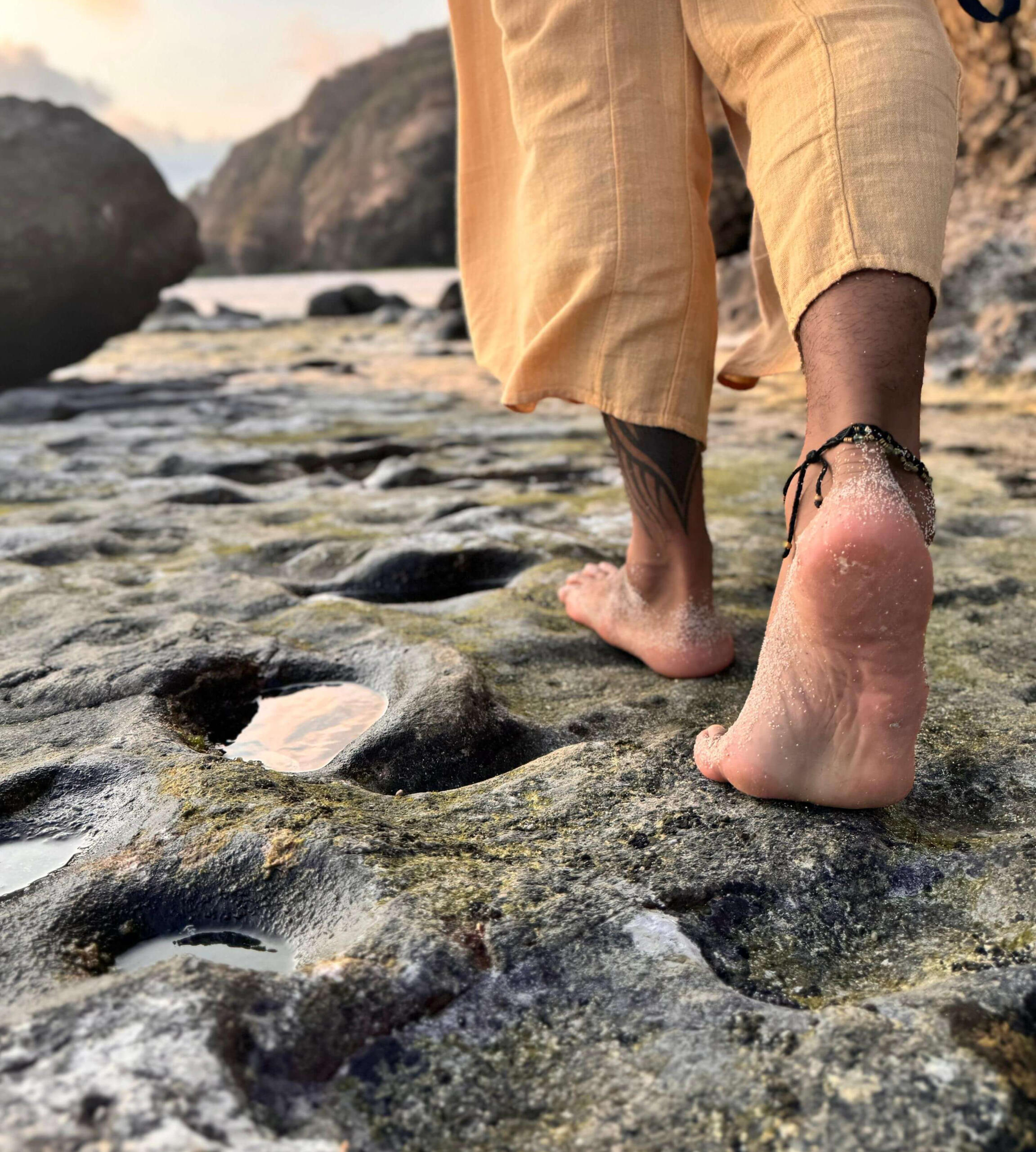 Transformational Coaching Journey – Free Lopez Walking Barefoot on Lomboks Earth Close-up of Free Lopez’s bare feet walking across water-filled rocks on a Lombok beach, symbolizing personal transformation, mindful steps, and connection to nature